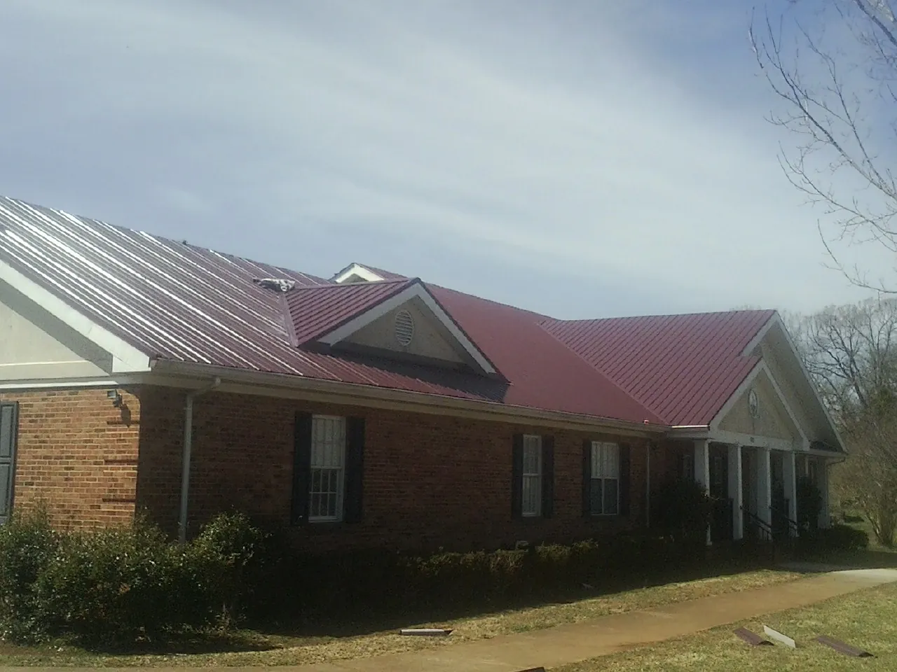 Red metal roof with gabled entries on a long brick building, from a Hail Damage Roof Repair job in Juliustown