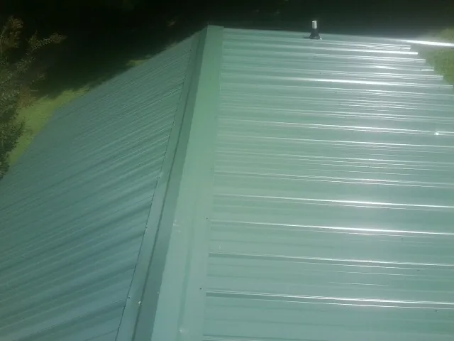 New green metal panels meeting at the ridge of a roof — Flat Roof Repair work by our crew in Juliustown