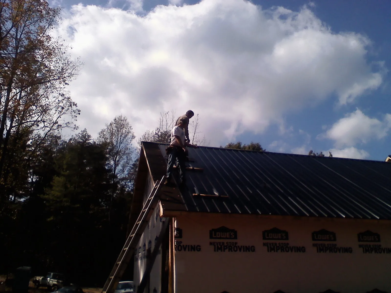 Roofer fastening dark metal panels high against a cloudy sky, from a Roof Inspection job in Juliustown