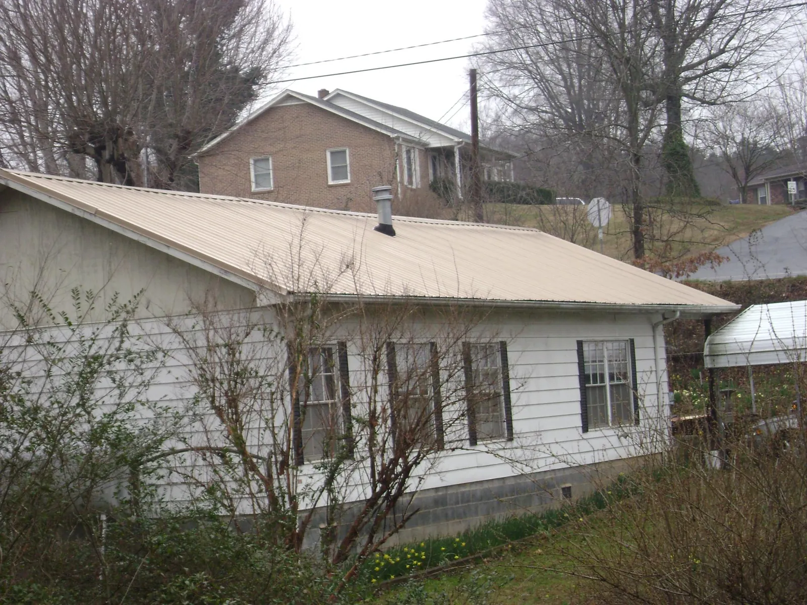 Tan metal roof on a white sided house set into a hillside — Commercial Roofing by Roofing Brothers in Juliustown